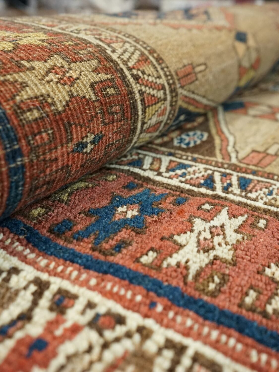 Close view of a hand-knotted rug rolled back on itself, showing the wool pile and a border of ivory and indigo motifs.